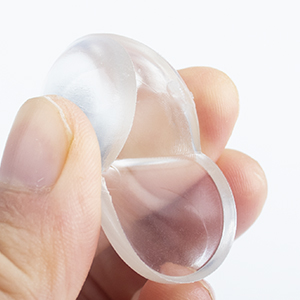 Clear, flexible silicone menstrual cup held between thumb and forefinger against a white background.