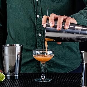 cocktail being poured into a coupe glass from a Boston shaker tin