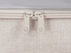 Close-up detail of a light beige or cream colored bag showing zipper compartment and textured fabric material.