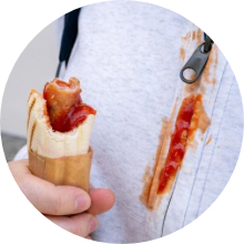 Close up of half eaten hot dog and stained shirt.