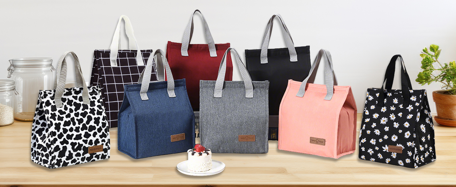 Collection of insulated lunch bags in various colors and patterns including cow print, denim blue, grey, red, black, pink, and polka dot designs, arranged on wooden surface.