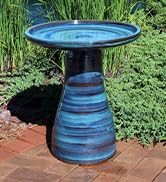 blue galaxy glazed ceramic bird bath on a brick patio near lush landscaping in the summer