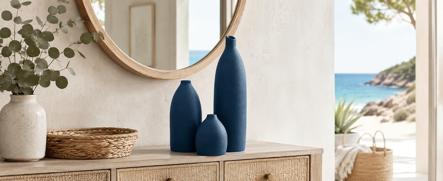 Matte navy blue vase set on an entryway console with woven accents, mirror, and ocean view.