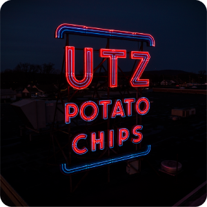 A glowing red neon UTZ POTATO CHIPS sign with blue accents stands against a dark, night sky.
