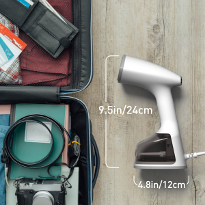 Handheld garment steamer with dimensions labeled: 9.5in/24cm height and 4.8in/12cm width. Shown next to an open suitcase containing folded clothes and accessories.