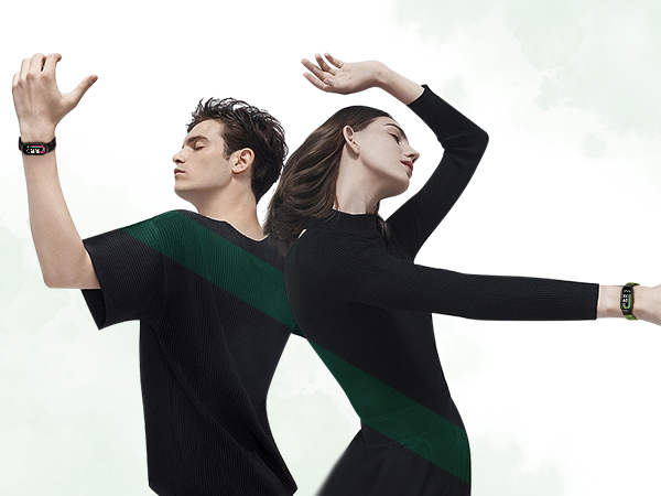 Two people wearing black and green athletic shirts, striking dynamic poses with arms raised. Both wear matching wristbands, suggesting a fitness or sports context.