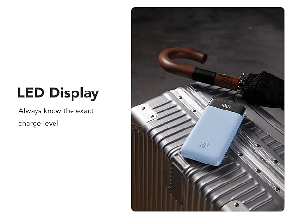 Blue portable device with LED display for charge level monitoring, shown resting on silver luggage with wooden handle visible.