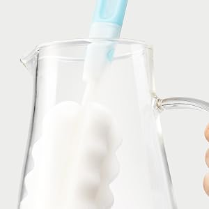a hand holding a toothbrush in a glass jug.