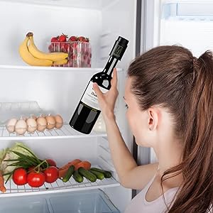 Interior of refrigerator showing fresh produce including bananas, strawberries, tomatoes, cucumbers, and eggs, with a wine bottle being placed on shelf.