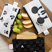 Reusable snack bags featuring Mickey Mouse with apple slices, and grapes on a cutting board