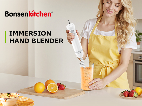 Bonsenkitchen immersion hand blender being used to blend orange liquid in a glass. Woman in yellow apron demonstrating use with fruits on counter.