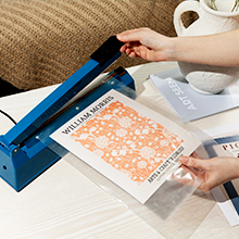 A pair of hands using an impulse sealer on our plastic sealable bags to package an art print