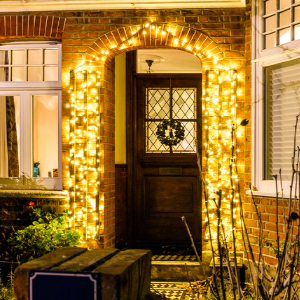 Porch entrance with warm string lights wrapped around doorway, illuminating a wreath on glass-paned door at night.