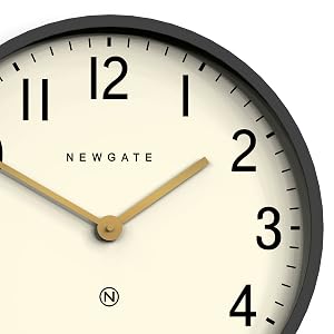 Newgate wall clock with black frame, cream-colored dial, and bold black numerals. Features brass-colored hands and modern minimalist design.