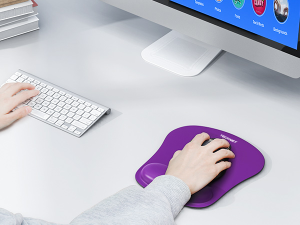 Purple ergonomic mouse pad with wrist rest on a desk, next to a white keyboard and computer mouse. Hand shown using the mouse pad.