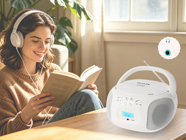 Girl with white headphones listening to CD player while reading on sofa.