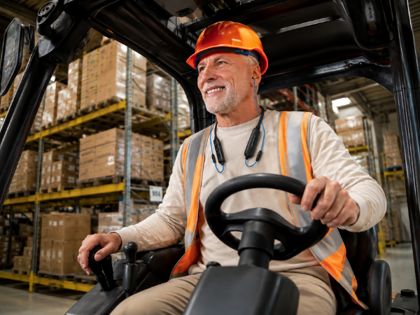 An old man wearing the HomeSpot Neckband while driving Forklift at the Warehouse