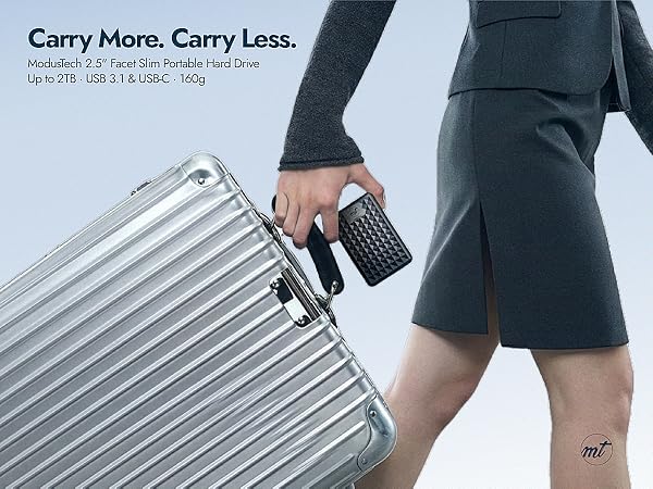 Woman in grey suit walking with silver suitcase holding ModusTech Facet portable hard drive in black