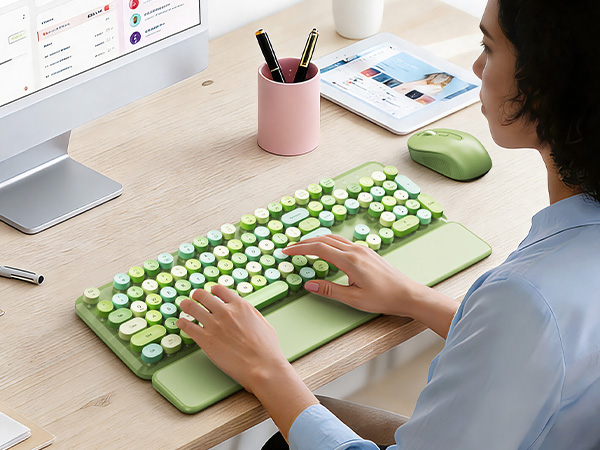 Person using green keyboard with wrist rest and mouse at a clean desk workspace