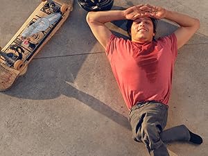 Hand-skater in red shirt and gray pants lies on concrete.