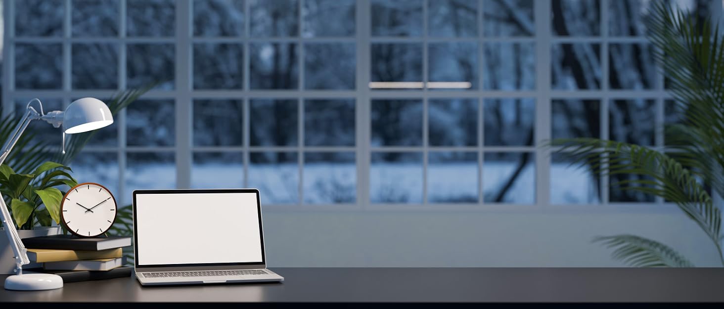 Modern office desk setup with laptop, desk lamp, and plant against window background with city view.