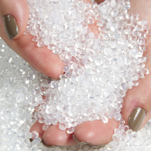 Close-up of hands with painted nails touching small, clear, spherical pellets or beads scattered on a white surface.