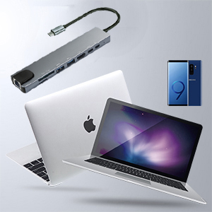 Electronic devices including laptop, smartphone, and USB hub arranged on white surface. Laptop displays purple background image.