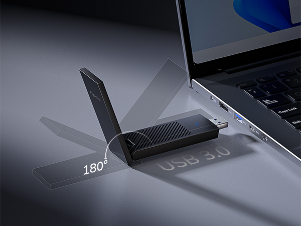 Close-up of black wireless device with 180-degree adjustable antenna against laptop keyboard in low-light setting.