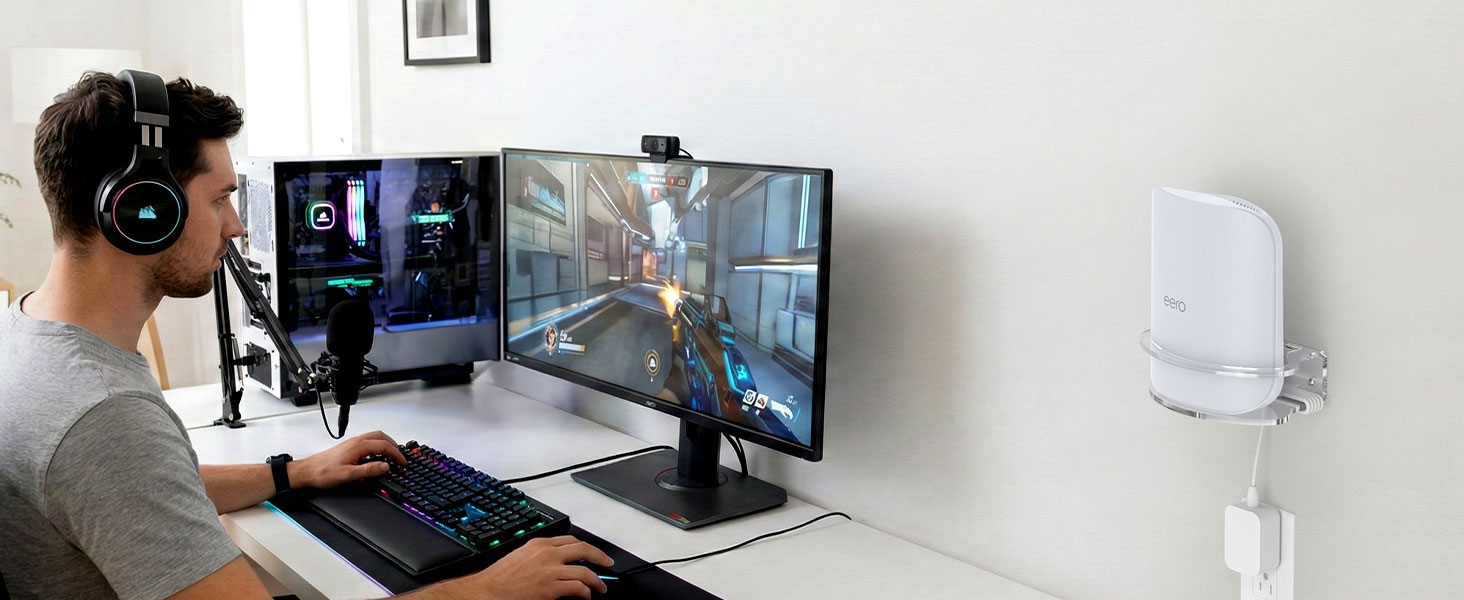 Person at desk setup with dual monitors and VR headset, gaming or working in virtual environment with white device mounted on wall.
