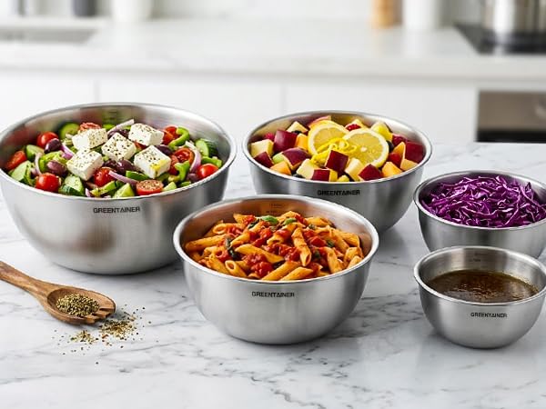 Five stainless steel mixing bowls containing various food ingredients: salad greens, sliced vegetables, purple cabbage, orange noodles, and liquid, arranged on marble surface.