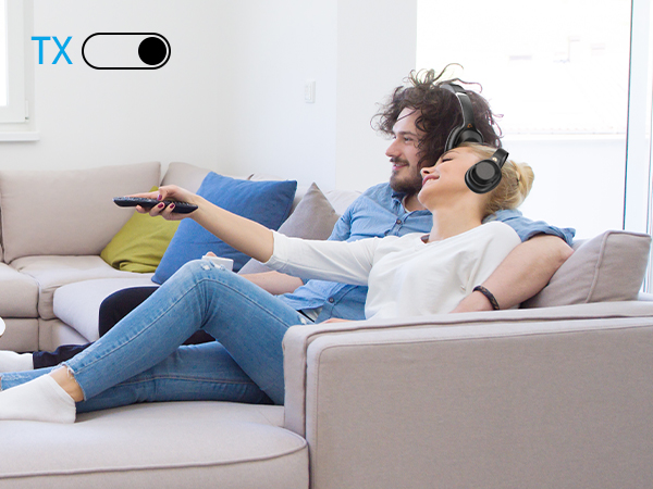 Two people sitting on a couch, wearing headphones, holding remote controls. 'TX' toggle switch visible in top left corner.