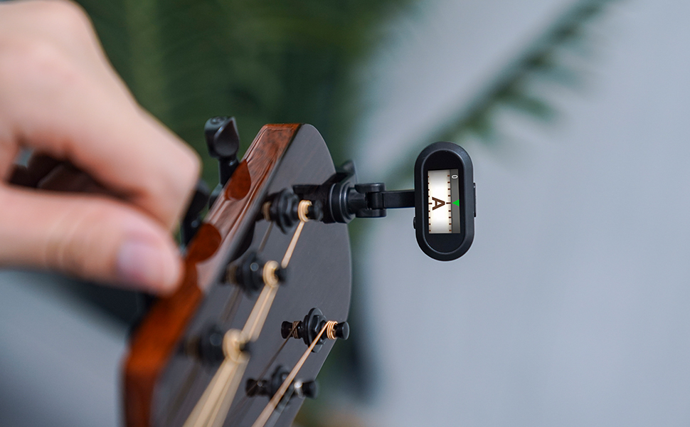 Close-up of a guitar headstock with a small digital tuner clipped onto a tuning peg. The tuner's display is visible.