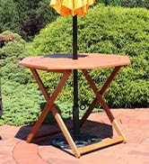 meranti wood folding outdoor patio table with umbrella hole on a brick patio with lush landscaping