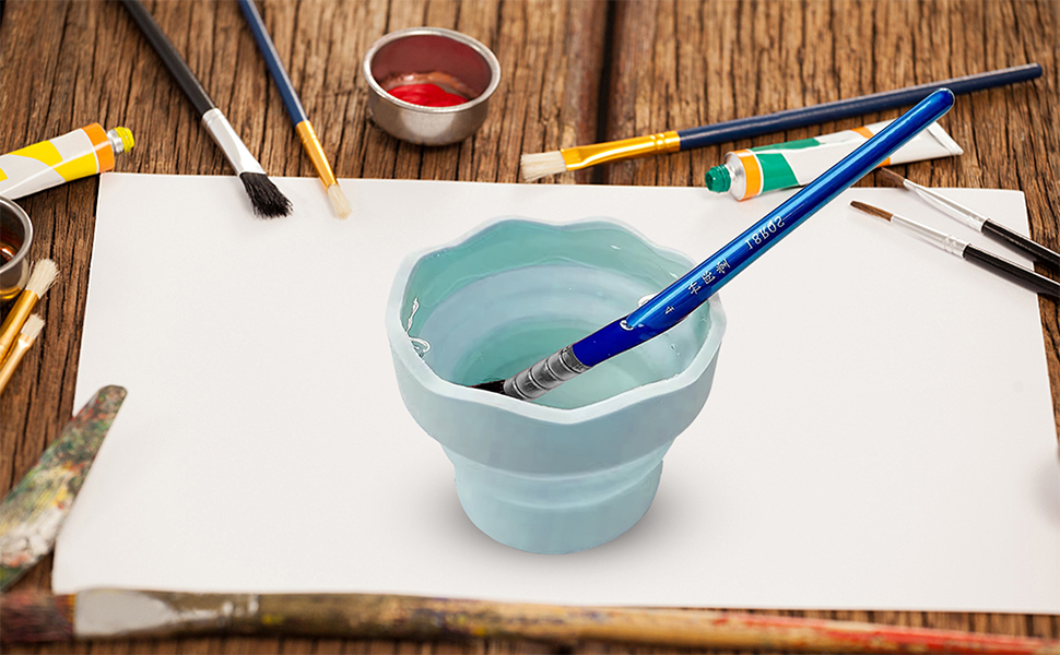 Light blue collapsible water cup for art supplies, shown with paintbrushes and art materials on wooden surface.