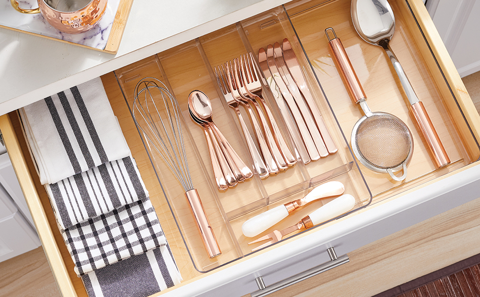 clear drawer organizer holding towels, whisk, spoons, forks, knives in wood drawer, white cabinet