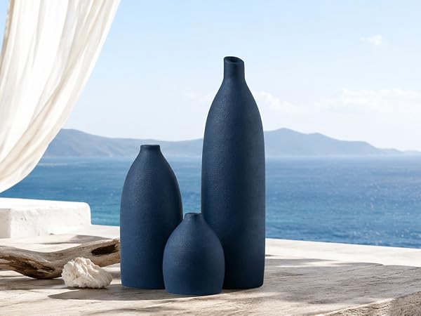 Matte navy blue vase set on an entryway console with woven accents, mirror, and ocean view.