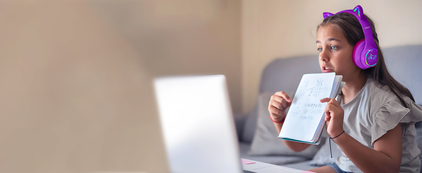 Purple over-ear headphones worn by person looking at laptop screen. User holds notebook and pen, suggesting use for remote work or online learning.