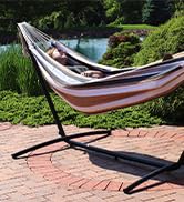 Woman laying in double brazilian hammock with stand on a brick patio with lush landscaping and pond
