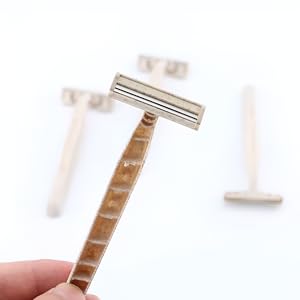 Close-up of a hand holding a single razor with three razors blurred in the background