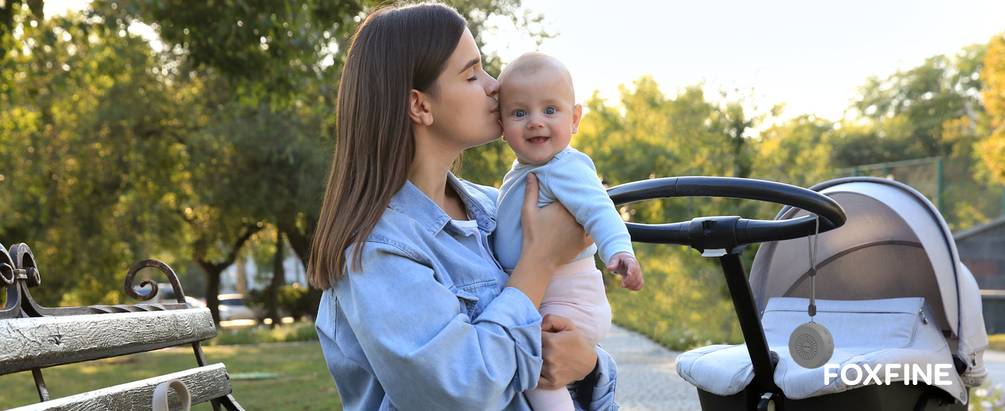 Mother clipping FOXFINE sound machine to stroller outdoors