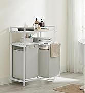 White metal bathroom storage unit with two shelves and fabric compartment. Features towel bar and holds toiletries. Positioned against white wall in bathroom setting.