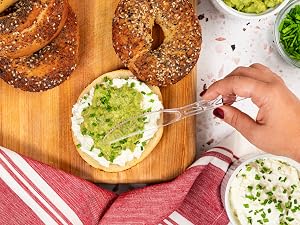 Plastic knife spreading guac over a bagel.