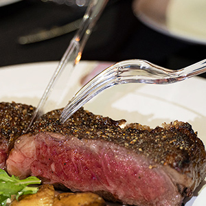 a clear knife and clear fork are cutting the steak