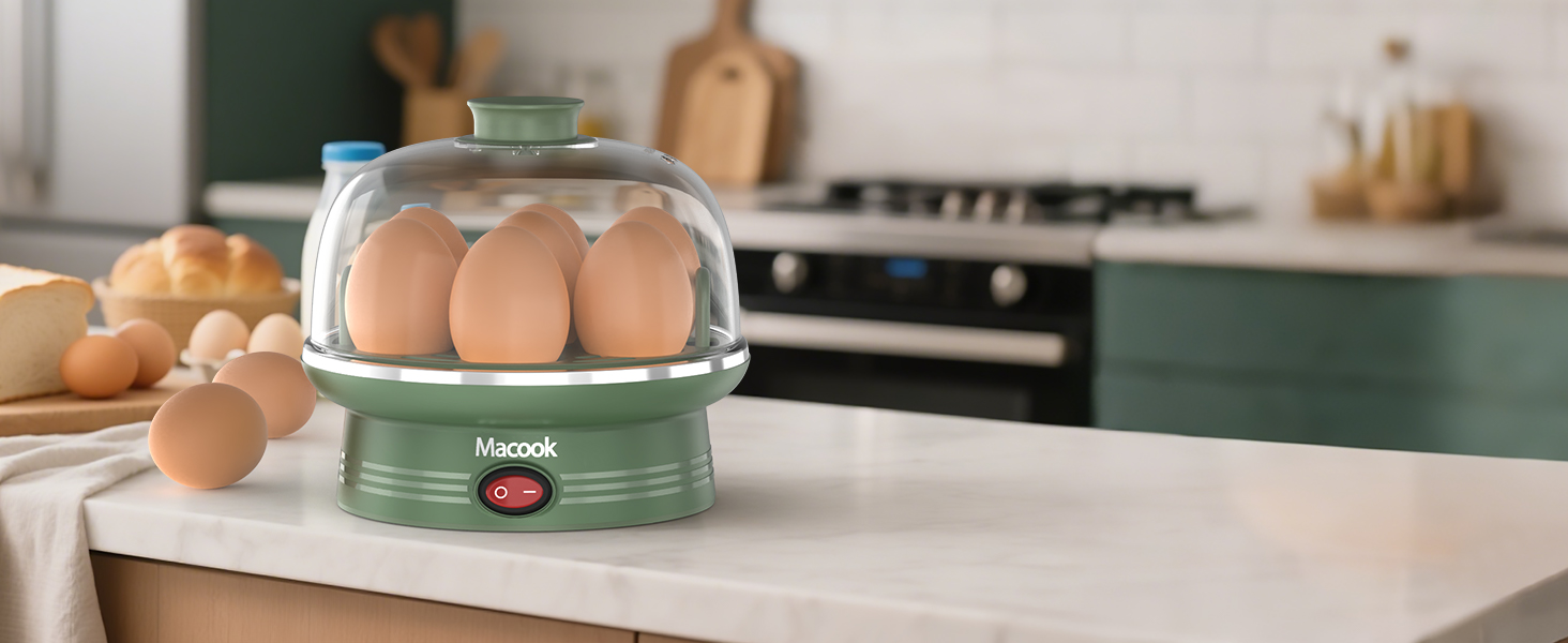Electric egg cooker with transparent dome lid on kitchen counter. Device has green base, holds multiple eggs, and is surrounded by additional eggs on the counter.
