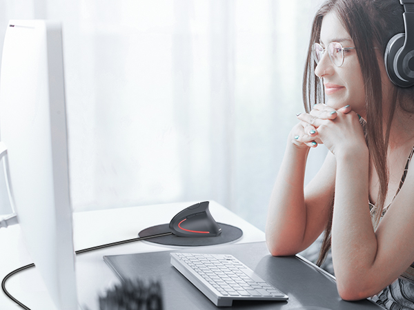 Person wearing headphones at desk setup with monitor, keyboard, and record player in bright, window-lit space.