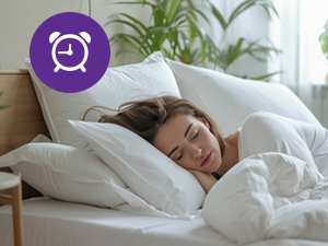 Woman sleeping peacefully in a white bed with fluffy pillows and comforter. Purple icon with alarm clock silhouette overlaid in top-left corner.
