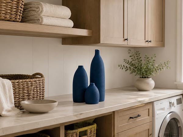 Coastal blue ceramic vase set on a laundry room countertop with natural wood cabinets.