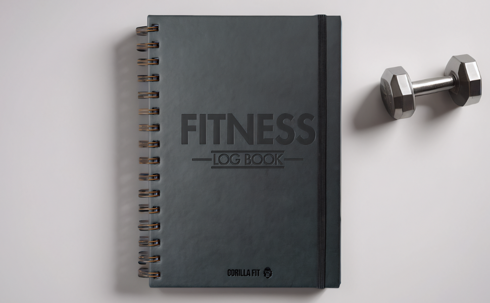 Gray spiral-bound fitness logbook with embossed 'FITNESS' text on cover, alongside a small metal dumbbell on white surface.