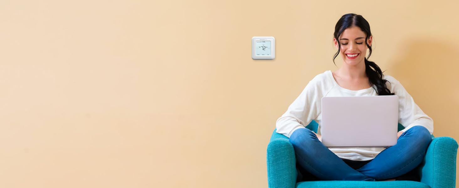 Woman using laptop computer in chair, thermostat installed on wall to her right