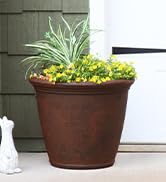 Large brown garden planter in front of garage door in front yard full of lush flowers and plants
